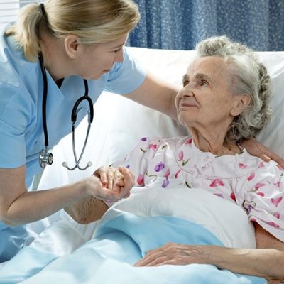 Lady caregiver providing comfort to elderly lady in bed.