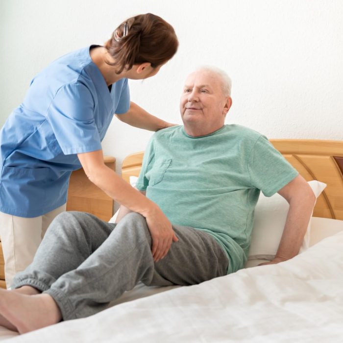 A medical professional helps an elderly guy go into bed.
