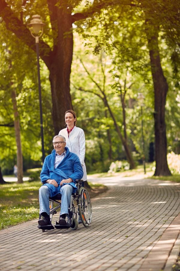 Female caregiver accompanies elderly person in wheelchair.