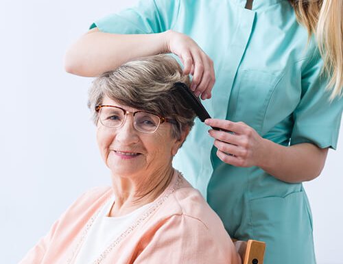 Caregiver affectionately brushing hair of senior woman.